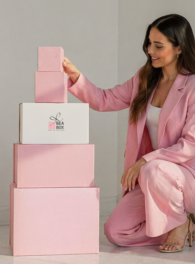 Žena u ružičastom odijelu slaže personalizirane ružičaste i bijele ukrasne kutije za poklone.